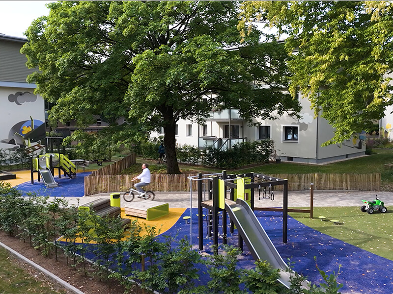 Modernisiertes Wohnquartier mit Spielplatz; ein  Mann fährt mit dem Fahrrad durch die Anlage