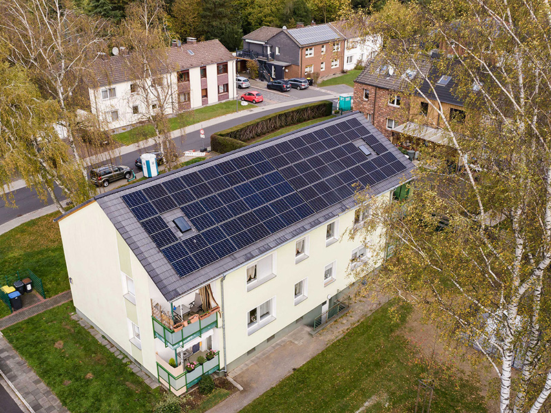 Mehrfamilienhaus von oben. Auf dem Dach befinden sich Photovoltaik-Anlagen